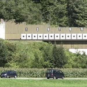 Швейцарский тир, где стрельба ведётся над оживлённым шоссе. Со стрелковых позиций видны только мишени, а автомобили скрыты бруствером от глаз стрелка.